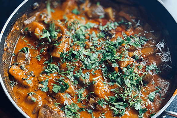A dish of food with a red sauce and garnished with green herbs.