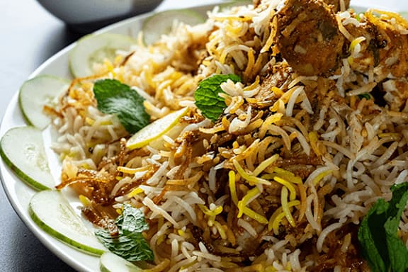 A plate of biryani with cucumber slices and mint leaves.