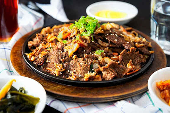 A dish of beef with vegetables and garnish on a wooden plate.
