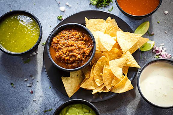 A plate of nachos with guacamole, salsa, and cheese sauce.