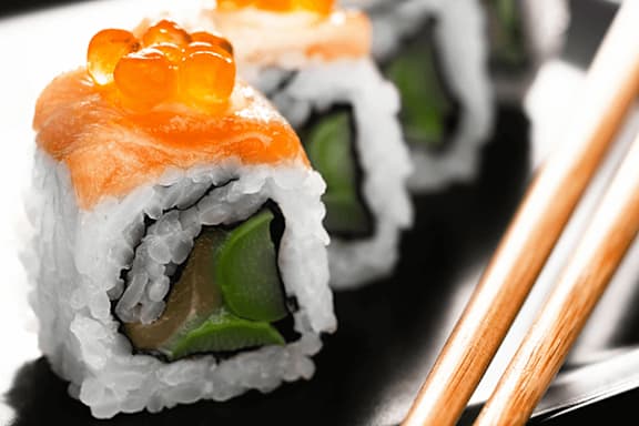 Sushi rolls with salmon and roe topping on a black surface.