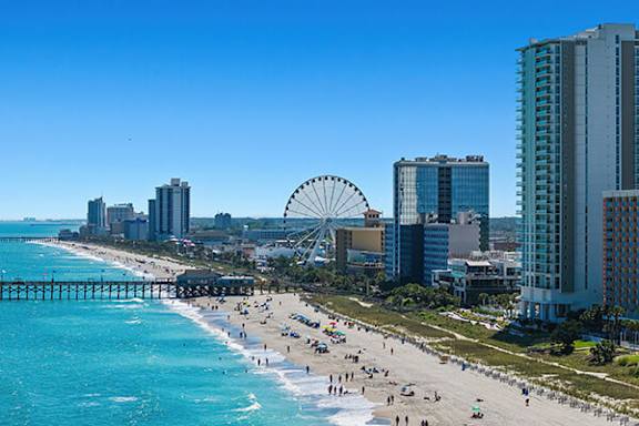A beach with a pier and a Ferris wheel in the background.