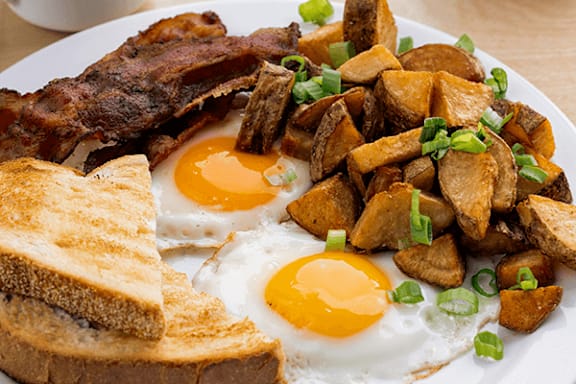 A breakfast plate with eggs, bacon, toast and potatoes.