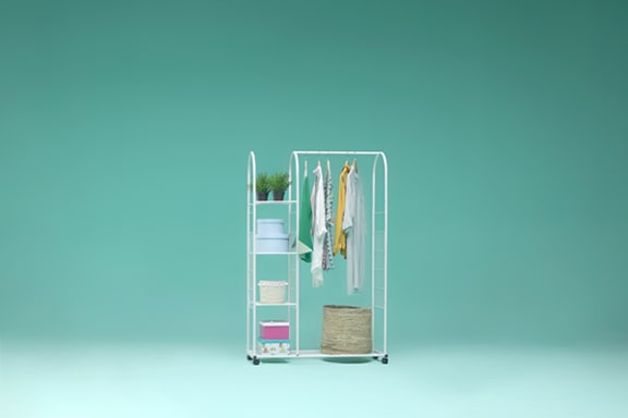 a metal shelving unit with clothes hanging on it and a basket on the bottom