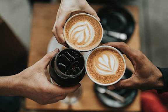 Three people holding cups of coffee with latte art on top.