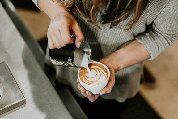 A person is making a latte art on a cup of coffee.
