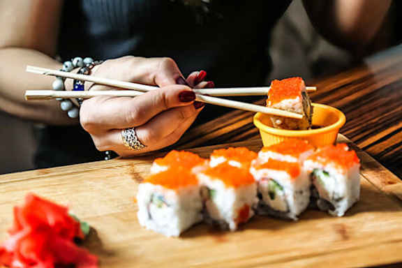 A person is holding chopsticks over a plate of sushi.
