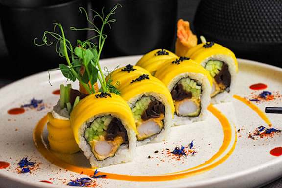A plate of sushi rolls with a yellow sauce drizzled on it.