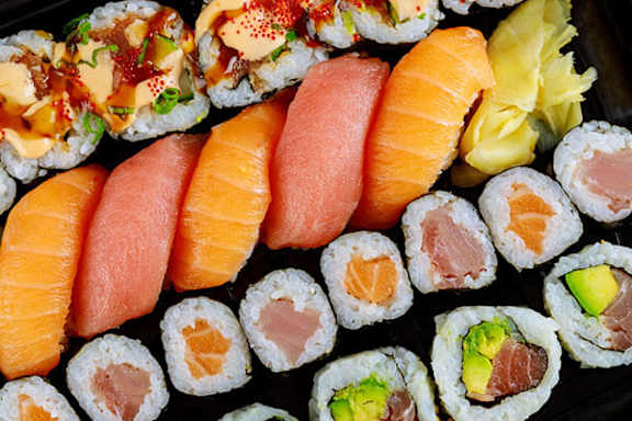 A variety of sushi rolls are neatly arranged on a black plate.