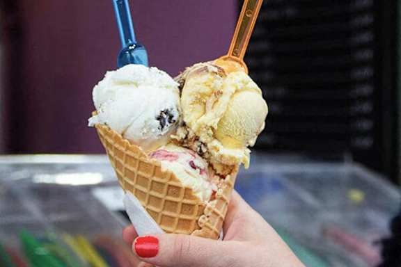 A hand holding a waffle cone with three scoops of ice cream.