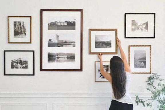 A woman is hanging pictures on a wall.