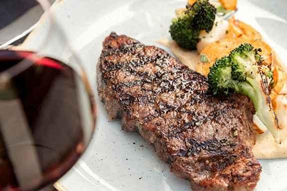 A steak with broccoli and carrots on a white plate.