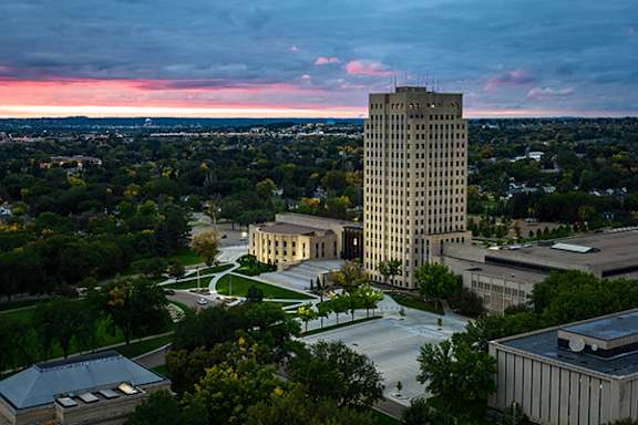 A tall building stands in the center of a campus with other buildings and trees around it.