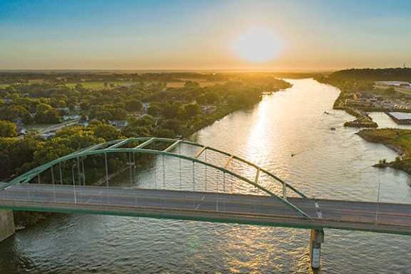 a bridge over a river with the sun setting over the water