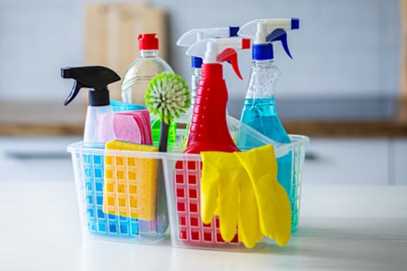 A basket full of cleaning supplies including spray bottles and gloves.