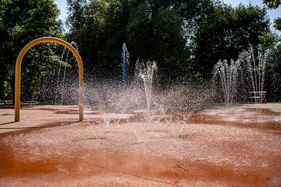 A water fountain with a yellow arch and a blue pole is spraying water.