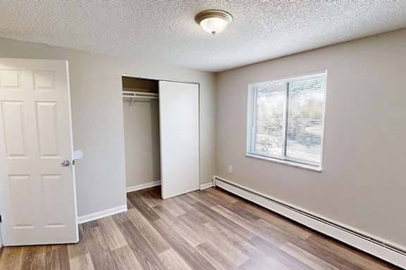 A room with a white door, a window, and a wooden floor.