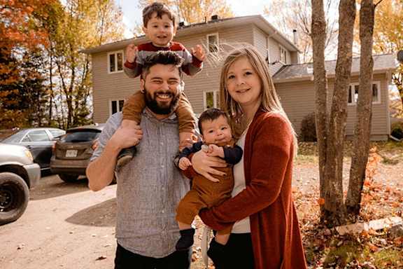 A family of four standing in front of a house.