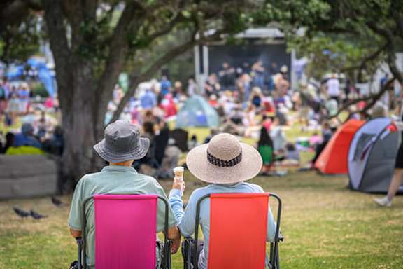 Two people sitting in chairs with a crowd in the background.