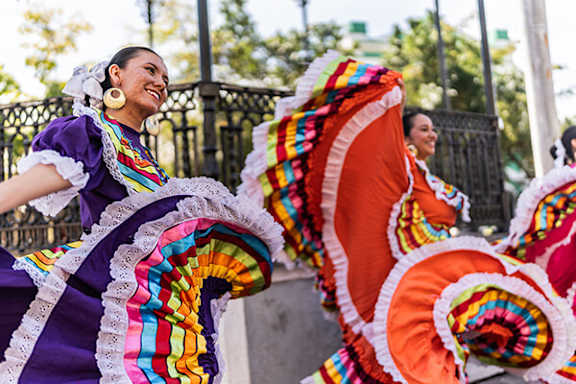 A woman in a purple dress with a colorful skirt is smiling.