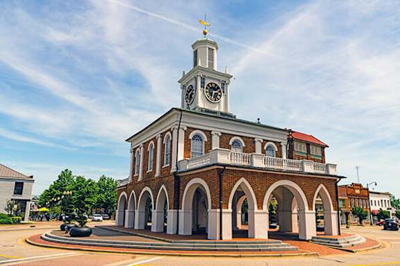 A clock tower stands atop a building with arched windows.