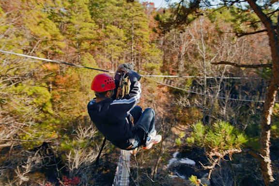 A person wearing a red helmet is ziplining through a forest.