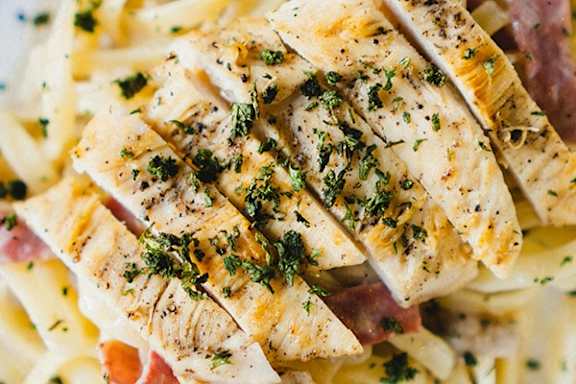 A close up of a plate of food with fish, pasta and ham.