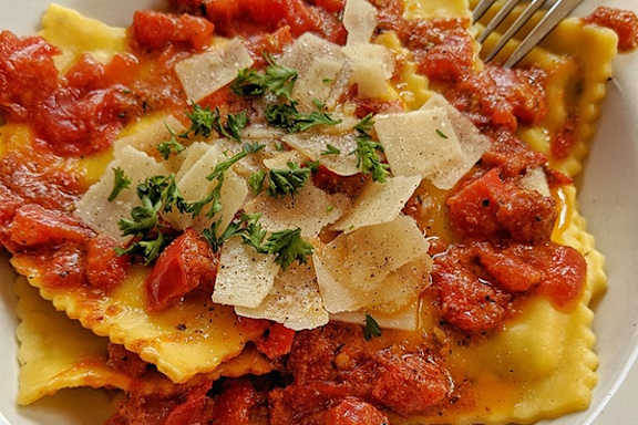 A plate of ravioli topped with tomato sauce and cheese.