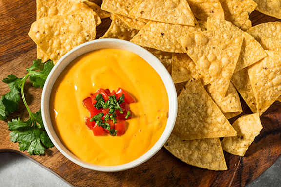 A bowl of orange dip surrounded by tortilla chips.