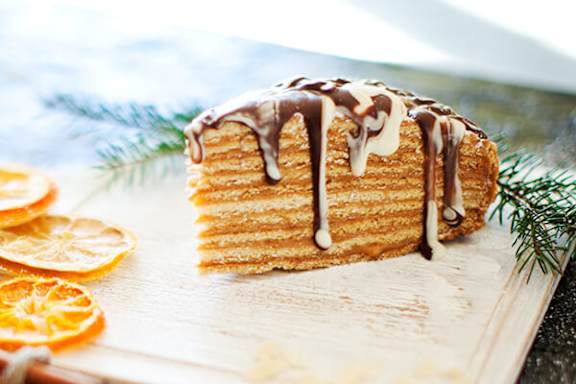 A piece of cake with chocolate sauce on top is on a wooden board.