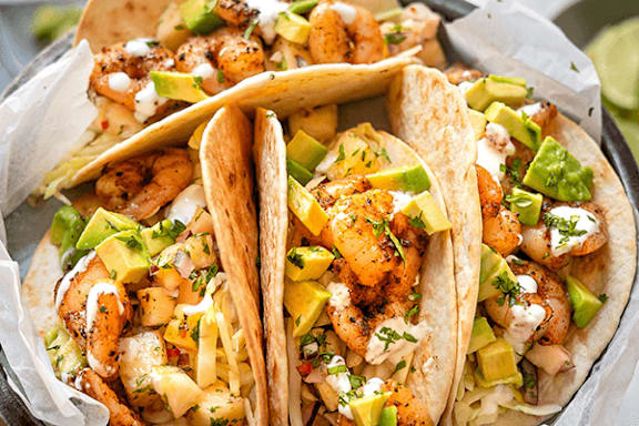 Three tacos filled with shrimp, avocado, and pineapple.