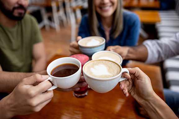 Four people toasting with cups of coffee.