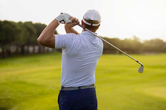 A man in a white shirt and blue pants is playing golf.