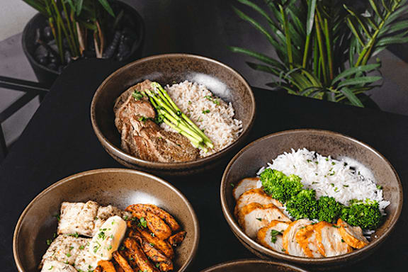 A meal is served in three bowls, one with rice and broccoli, another with meat and vegetables, and the third with fish and vegetables.