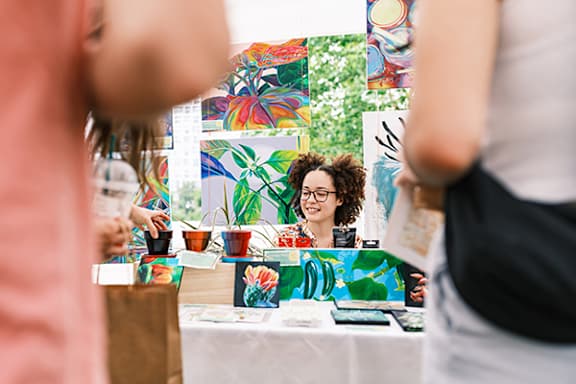 A woman with curly hair is standing behind a table with a colorful painting on it.