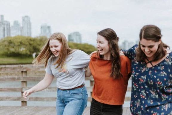 three girls laughing while walking by a river