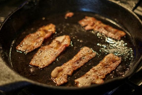 four pieces of bacon frying in a frying pan