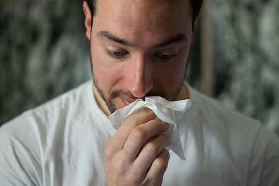 A man in a white shirt is blowing his nose into a tissue.