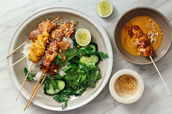 A plate of food with skewers and a bowl of sauce.
