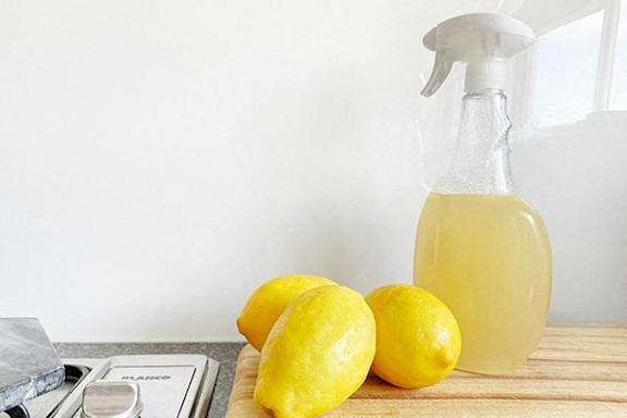 a bottle of lemon juice and three lemons on a cutting board