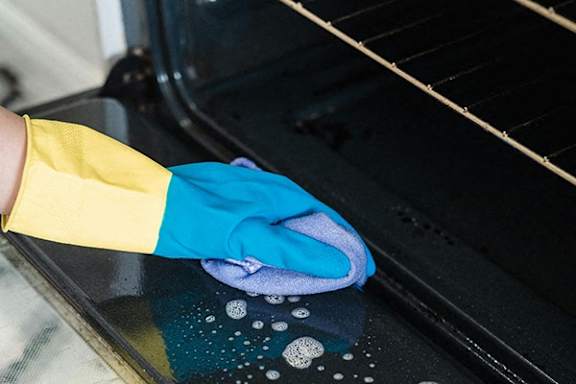 a hand with a blue and yellow glove cleaning an oven with a towel on the
