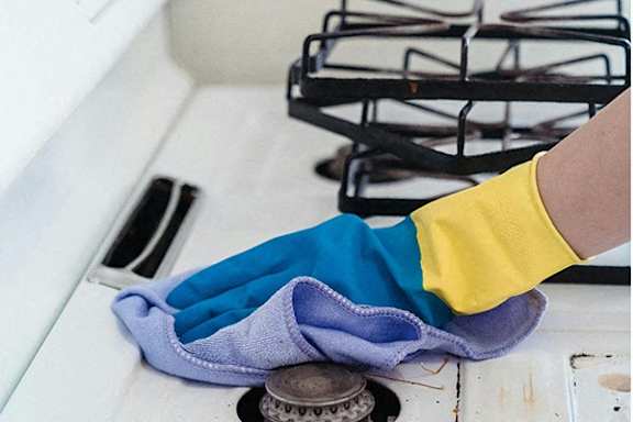 a person wearing gloves cleaning a stove with a towel on the oven