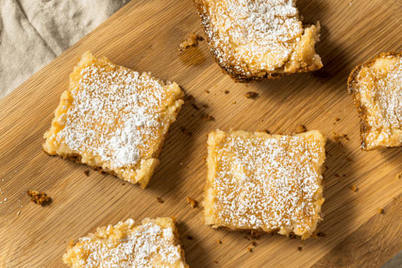 A wooden board with four square pieces of dessert sprinkled with powdered sugar.
