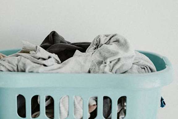 A light blue laundry basket filled with a pile of wrinkled clothes.