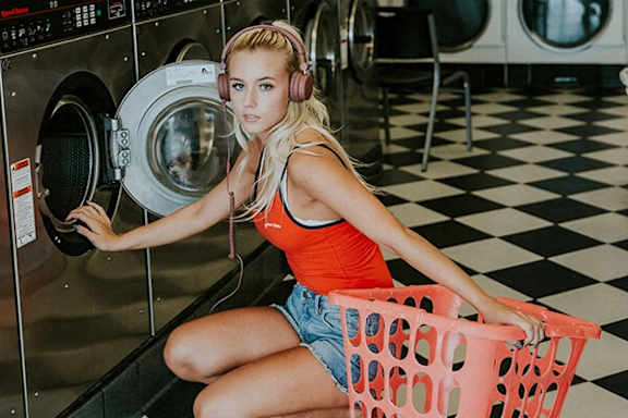 A woman in a red top and denim shorts is sitting in front of a washing machine.
