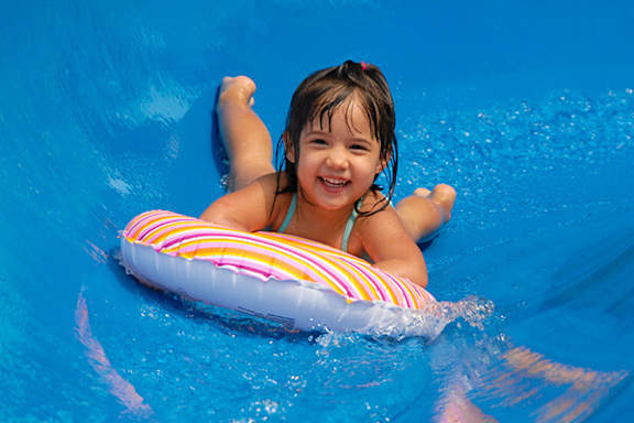 A little girl is smiling and floating on a colorful striped float in a blue pool.