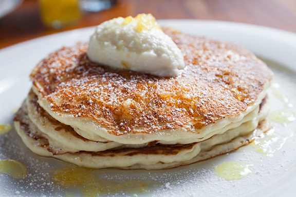 A stack of pancakes topped with a pat of butter and drizzled with syrup.