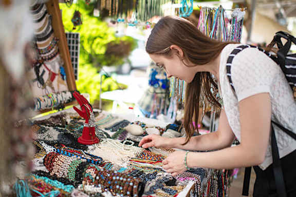 A woman is browsing through a variety of colorful beaded jewelry at a market stall.