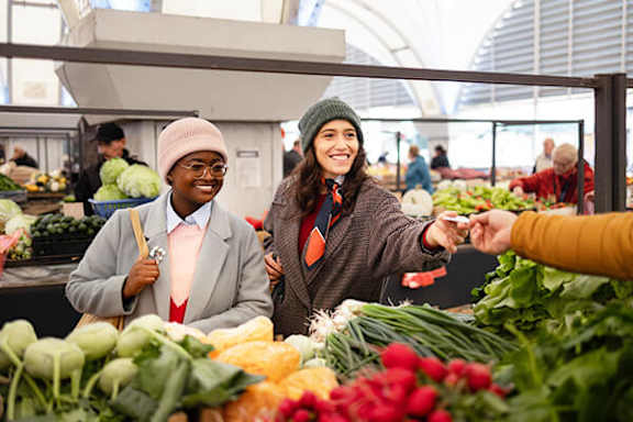 Two women shopping for vegetables at a market.