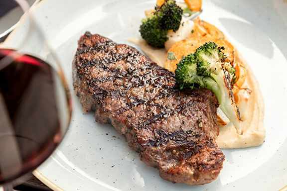 A steak with broccoli and carrots on a white plate.